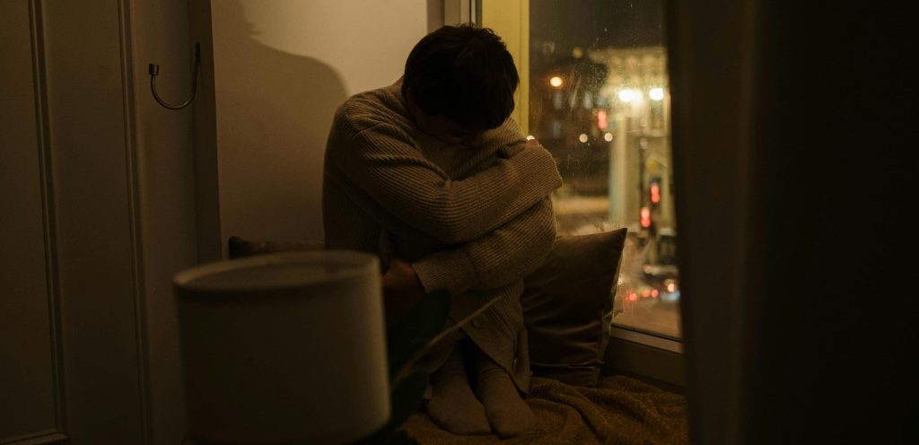 A person experiencing emotional exhaustion, sitting quietly by a window.