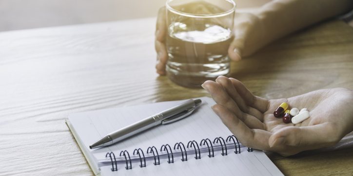Open journal beside hand holding antidepressants and a glass of water.