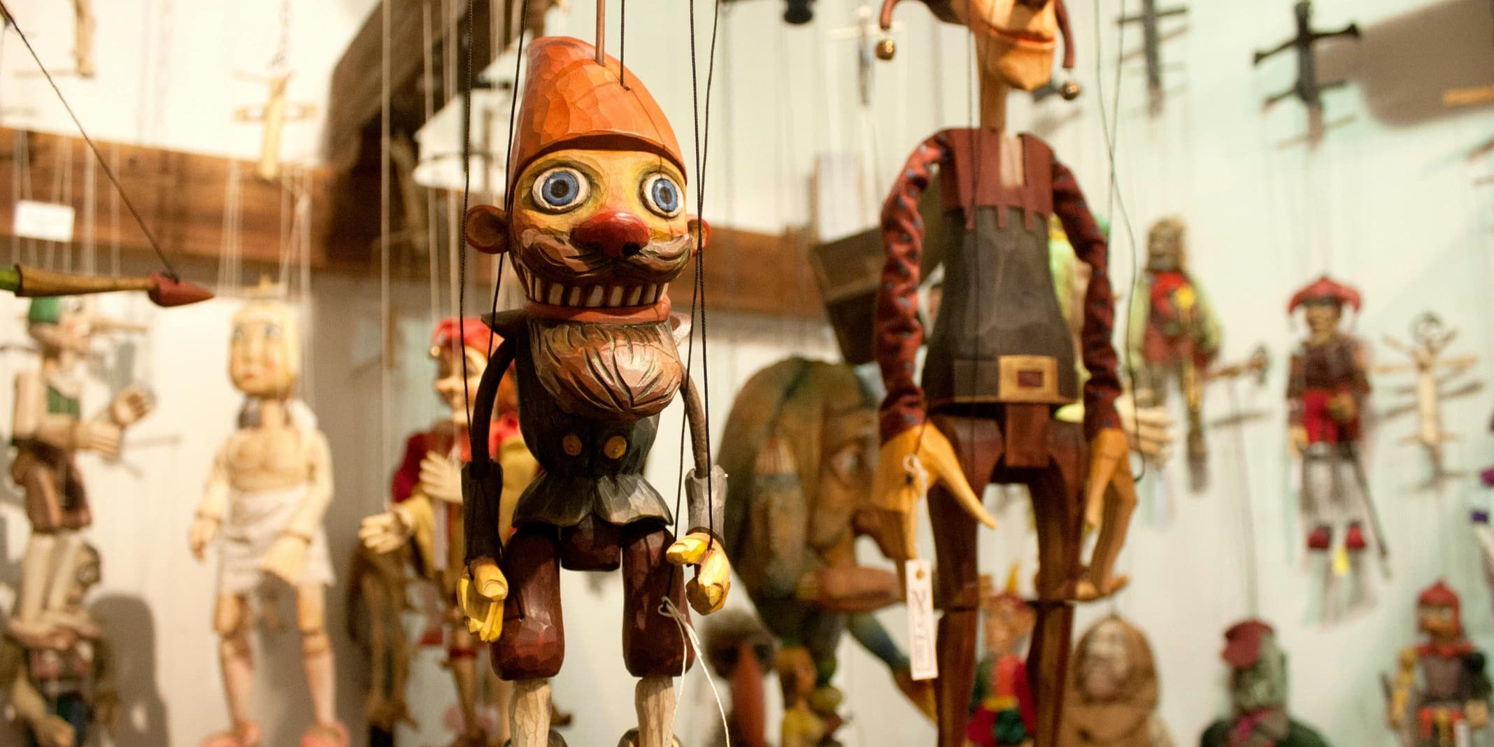 A collection of vividly painted wooden marionettes hanging by strings in a puppet workshop.