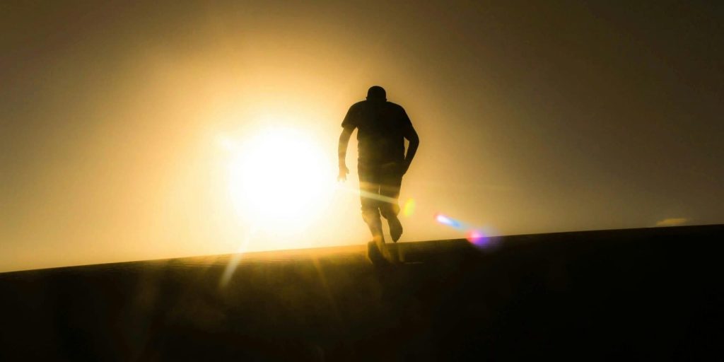 Silhouette of a man walking uphill into a blazing golden sun, symbolizing struggle and hope.
