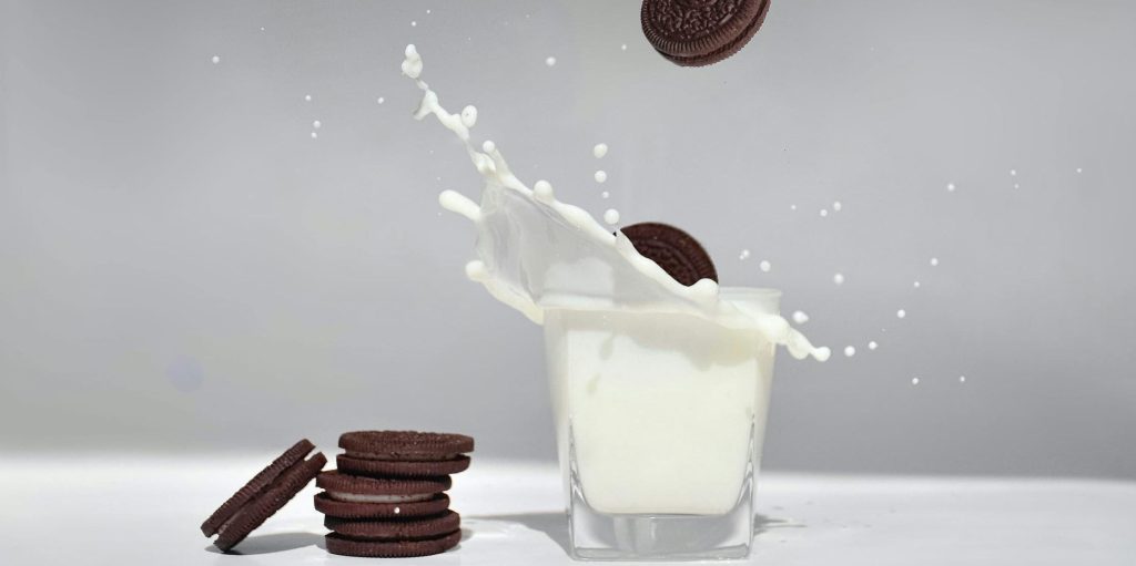 Several chocolate sandwich cookies captured mid-fall into a glass of milk, causing a dramatic splash.