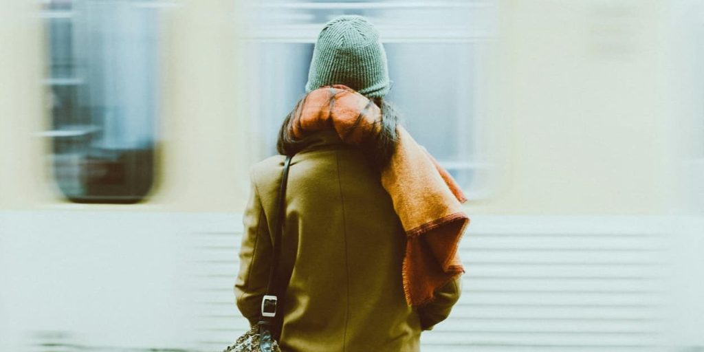 Person in coat and beanie standing on a platform as a train speeds past.