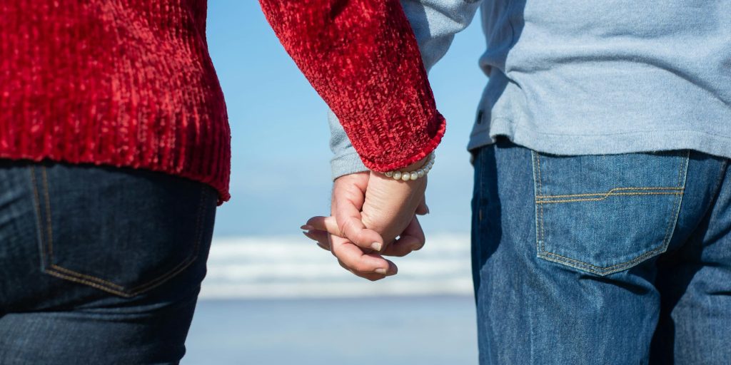 Close-up of a couple holding hands by the seaside, wearing casual clothes, symbolizing love, unity, and companionship.