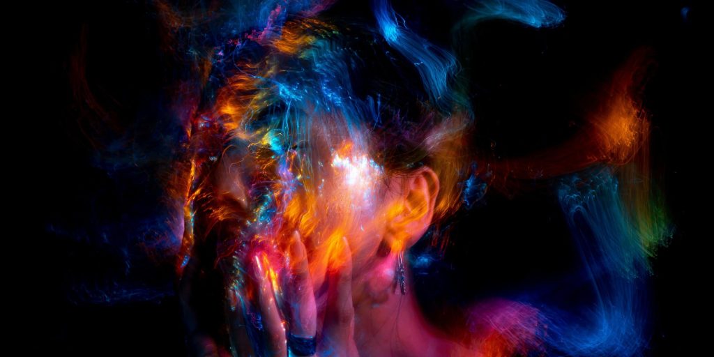 A blurred portrait of a person surrounded by swirling streaks of colorful light in blue, orange, and red tones.