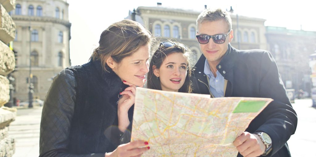 Three travelers studying a map together under bright sunlight in a historic city.