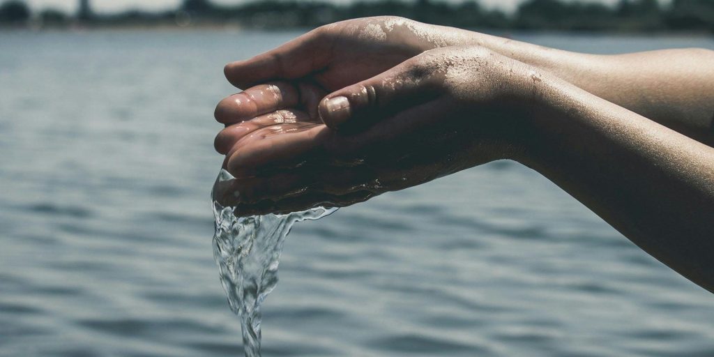 Two cupped hands releasing water back into a calm lake under daylight.