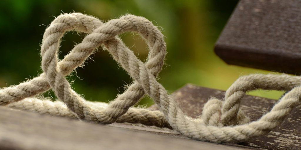 A close-up of a beige rope gently forming a heart shape on a wooden surface, symbolizing human connection and kindness.