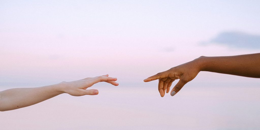 Two hands reaching across a pastel horizon, symbolizing connection and compassion.